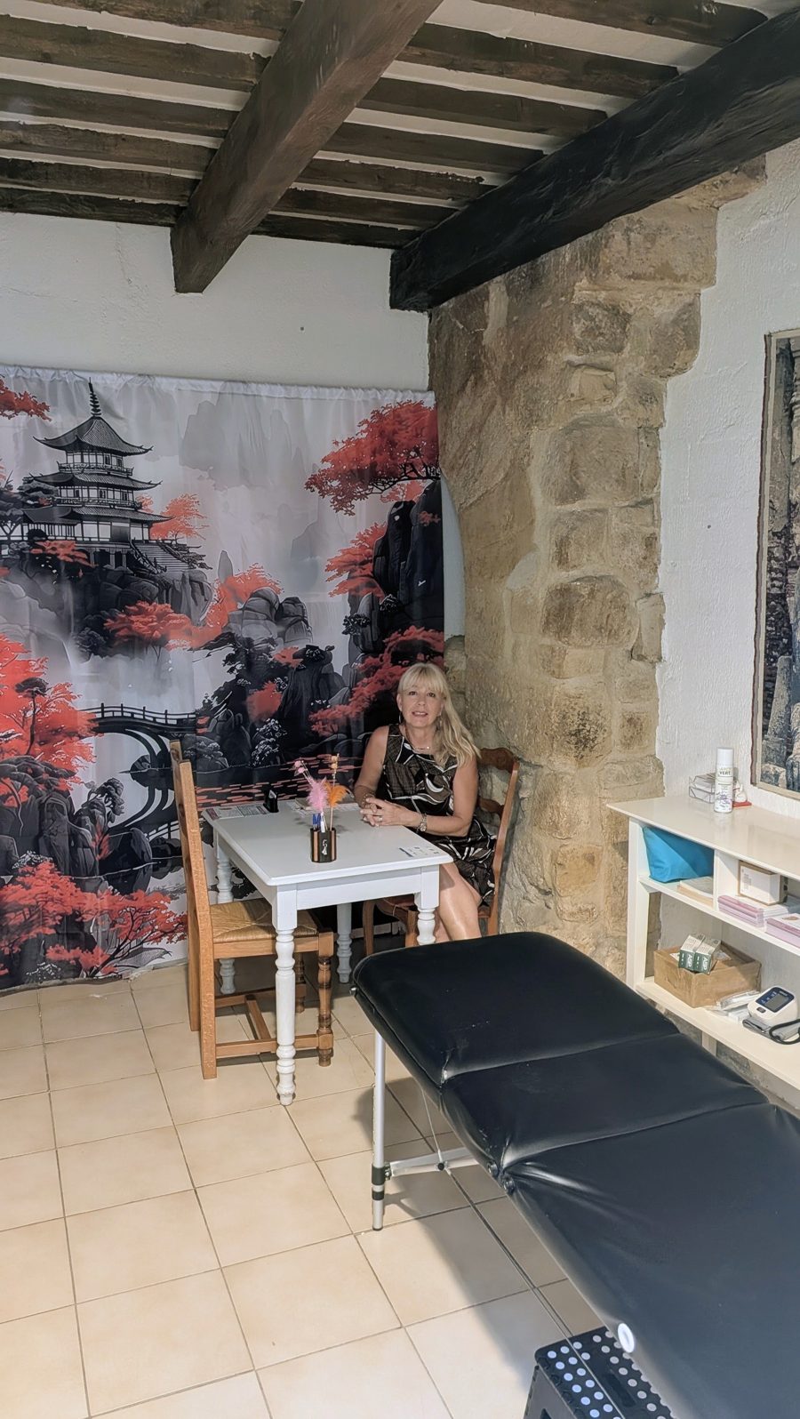 Isabelle André assise au bureau d'accueil du cabinet d'auriculothérapie de Florensac, devant une tenture japonaise